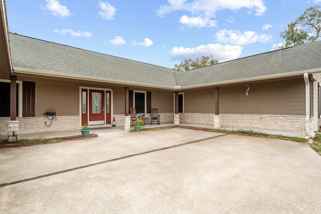 exterior space featuring covered porch, a shingled roof, and stone siding