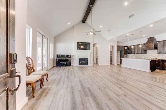 living area with ceiling fan, beam ceiling, a glass covered fireplace, light wood-type flooring, and visible vents
