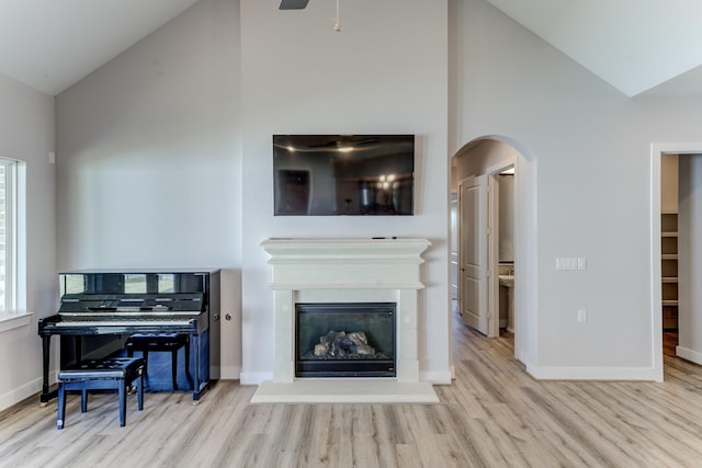 living room with arched walkways, high vaulted ceiling, a glass covered fireplace, baseboards, and wood finished floors