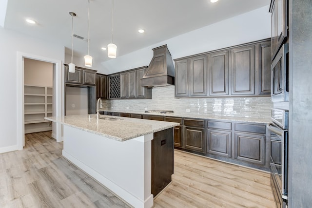 kitchen with a sink, light wood-style flooring, backsplash, and premium range hood