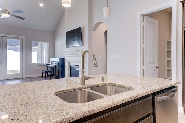 kitchen featuring a sink, a glass covered fireplace, lofted ceiling, arched walkways, and a ceiling fan