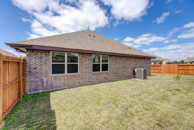 back of house with a shingled roof, brick siding, a fenced backyard, central air condition unit, and a yard