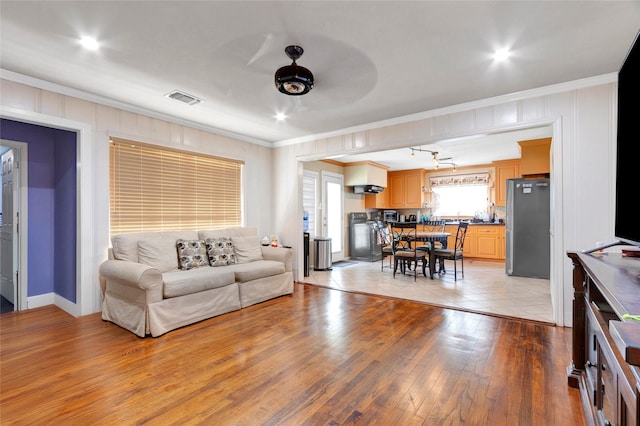living area featuring a ceiling fan, visible vents, ornamental molding, and light wood-style flooring