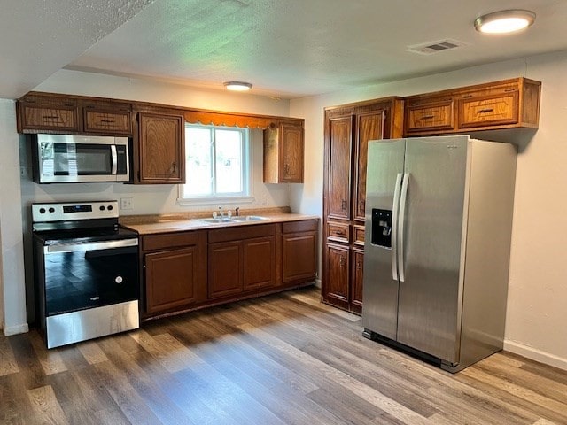 kitchen with visible vents, appliances with stainless steel finishes, wood finished floors, a sink, and light countertops