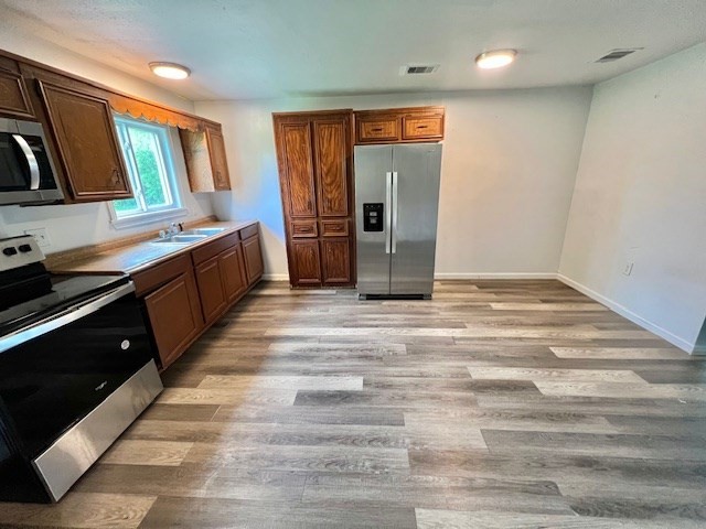 kitchen featuring visible vents, light wood-style floors, baseboards, a sink, and stainless steel appliances