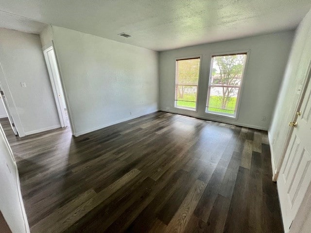 spare room with visible vents, a textured ceiling, dark wood finished floors, and baseboards