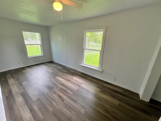 spare room featuring a healthy amount of sunlight, baseboards, a ceiling fan, and dark wood-style flooring