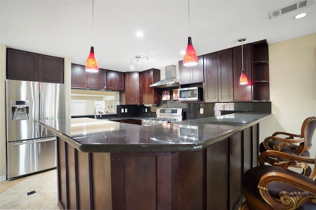 kitchen with wall chimney range hood, stainless steel appliances, decorative light fixtures, a peninsula, and visible vents
