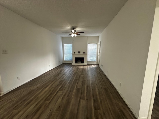 10047 Westpark Dr Unit 73, Houston, TX 77042 - unfurnished living room with baseboards, dark wood-type flooring, a fireplace with raised hearth, a textured ceiling, and a ceiling fan