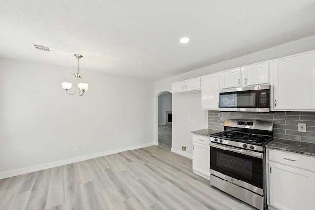 2707 Shawna Lyn Dr, Spring, TX 77373 - kitchen featuring dark stone counters, white cabinetry, arched walkways, light wood finished floors, and appliances with stainless steel finishes