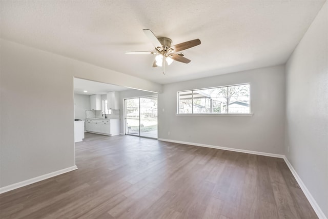 unfurnished living room featuring dark wood-style flooring, ceiling fan, and baseboards
