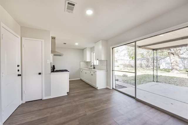 kitchen with white cabinets, dark wood-style flooring, wall chimney range hood, decorative backsplash, and visible vents