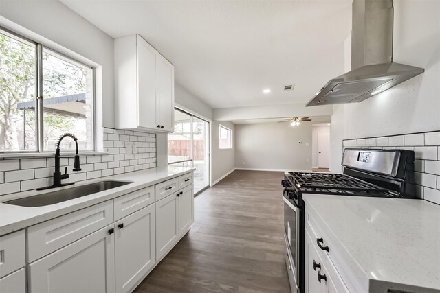 kitchen with a sink, wall chimney exhaust hood, stainless steel gas range oven, and decorative backsplash
