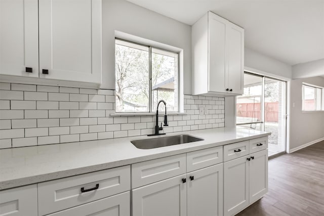 kitchen with tasteful backsplash, wood finished floors, a sink, baseboards, and white cabinetry