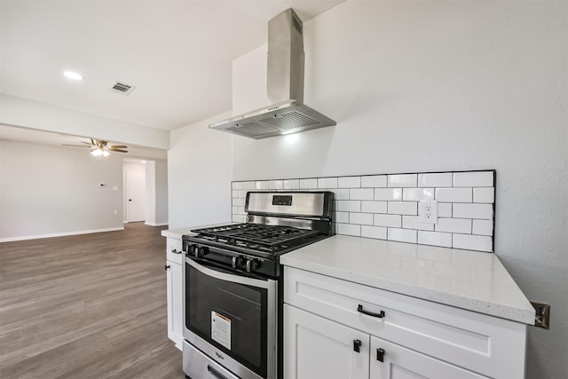 kitchen with wall chimney range hood, ceiling fan, visible vents, stainless steel gas range oven, and light wood finished floors