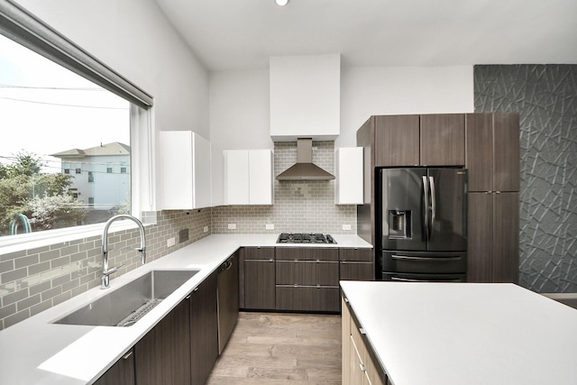 kitchen featuring light wood-type flooring, wall chimney exhaust hood, a sink, backsplash, and stainless steel appliances