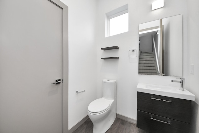 half bath with vanity, baseboards, wood finished floors, and toilet