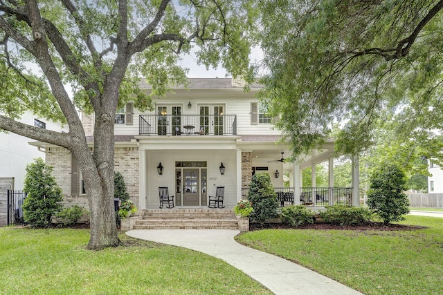 view of front of property featuring a balcony, a front yard, covered porch, french doors, and a ceiling fan