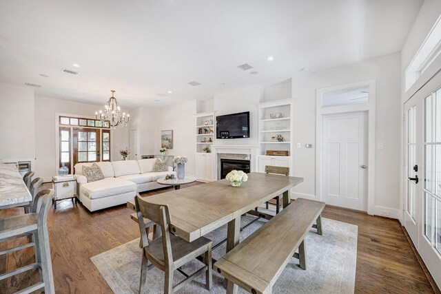 dining area with a notable chandelier, built in shelves, a high end fireplace, visible vents, and dark wood-style floors