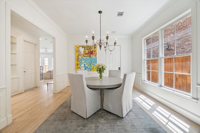 dining area featuring visible vents, crown molding, light wood-type flooring, an inviting chandelier, and a decorative wall