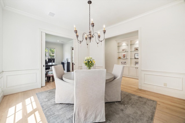 dining area with crown molding, a wainscoted wall, an inviting chandelier, a decorative wall, and light wood-style flooring