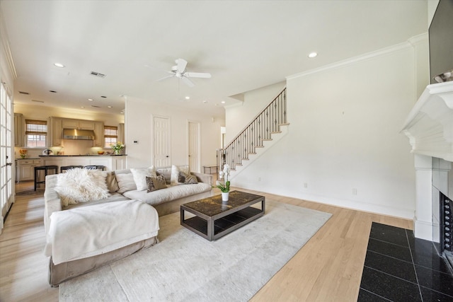 living area with visible vents, ornamental molding, stairs, ceiling fan, and a fireplace with flush hearth
