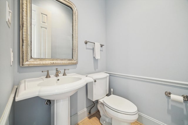 bathroom featuring baseboards, a sink, wood finished floors, and toilet