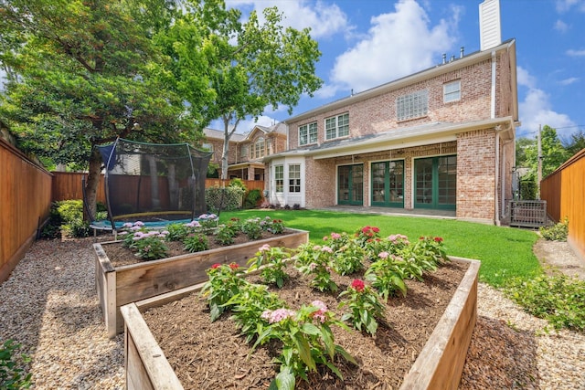 rear view of house featuring brick siding, a trampoline, a yard, and a vegetable garden
