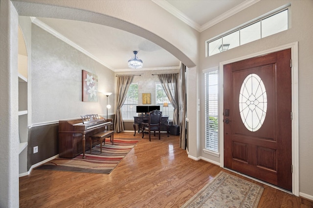 entryway featuring arched walkways, ornamental molding, baseboards, and wood finished floors