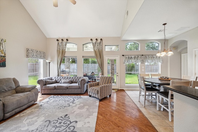 living area with visible vents, arched walkways, ceiling fan with notable chandelier, and high vaulted ceiling