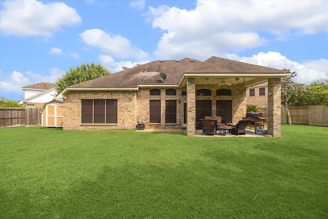 back of house featuring a shingled roof, a shed, a fenced backyard, a patio area, and a lawn