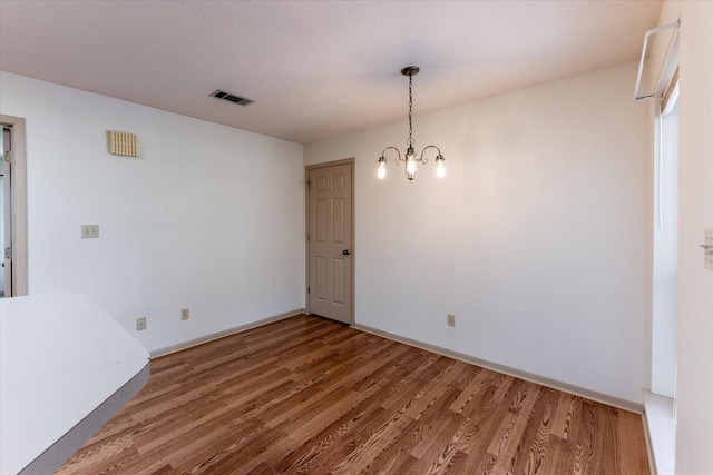 unfurnished dining area with baseboards, a chandelier, wood finished floors, and visible vents