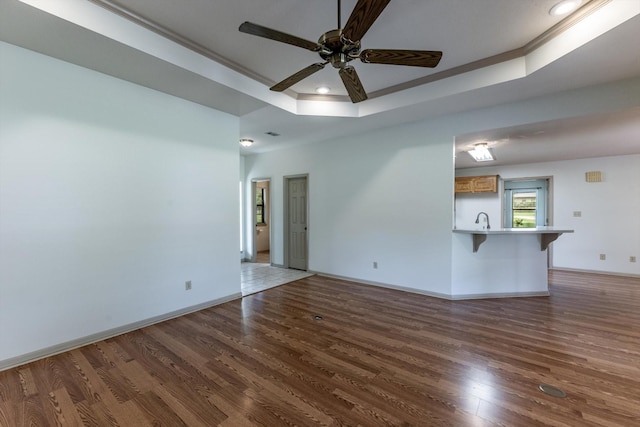 unfurnished living room with a sink, a raised ceiling, a ceiling fan, baseboards, and wood finished floors
