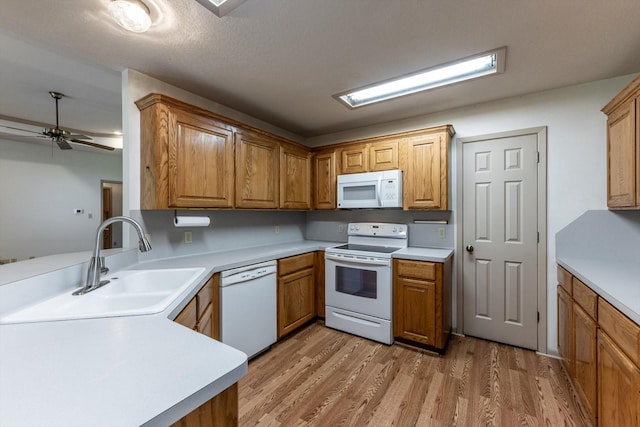 kitchen featuring a sink, light wood finished floors, white appliances, and light countertops