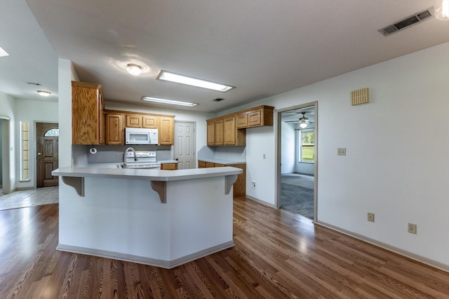 kitchen featuring a kitchen bar, visible vents, wood finished floors, a peninsula, and white appliances