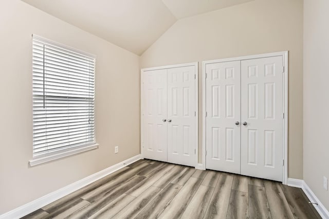 unfurnished bedroom with wood finished floors, baseboards, lofted ceiling, and two closets