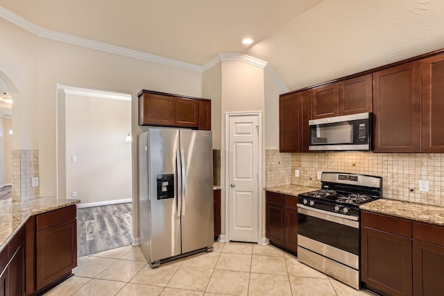kitchen featuring backsplash, appliances with stainless steel finishes, arched walkways, light stone counters, and ornamental molding
