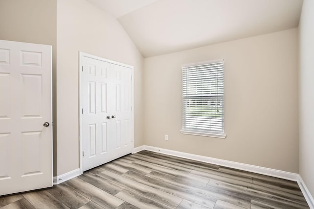 unfurnished bedroom with baseboards, lofted ceiling, wood finished floors, and a closet