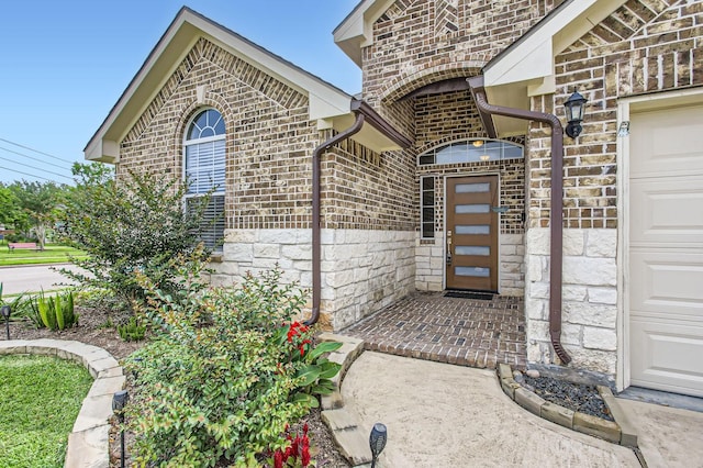 view of exterior entry featuring brick siding, an attached garage, and stone siding