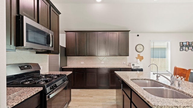 kitchen with dark brown cabinetry, tasteful backsplash, a sink, light wood finished floors, and stainless steel appliances
