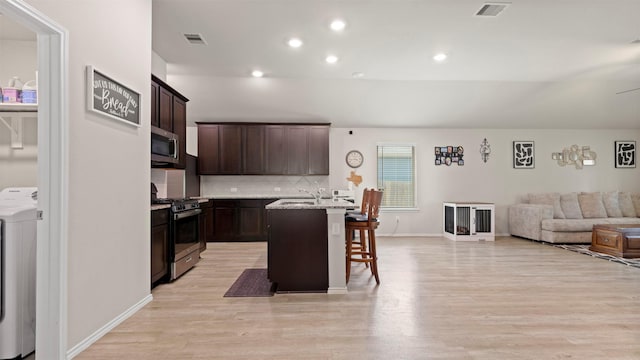 kitchen featuring a kitchen bar, washer / clothes dryer, appliances with stainless steel finishes, open floor plan, and light wood-style flooring