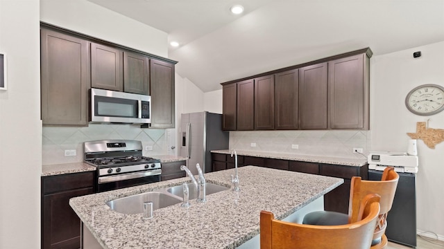 kitchen with dark brown cabinetry, appliances with stainless steel finishes, a sink, and lofted ceiling
