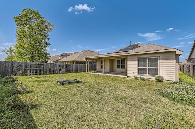rear view of house with a ceiling fan, solar panels, a lawn, a fenced backyard, and a patio