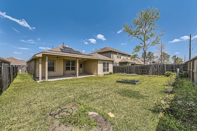 rear view of property with a fenced backyard, a ceiling fan, solar panels, and a patio area