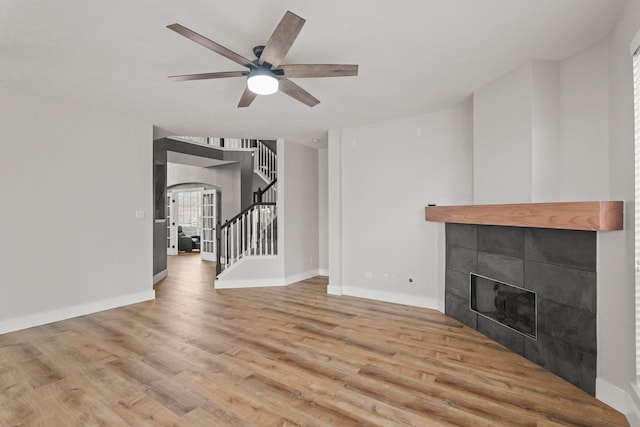 unfurnished living room with baseboards, ceiling fan, wood finished floors, and stairway