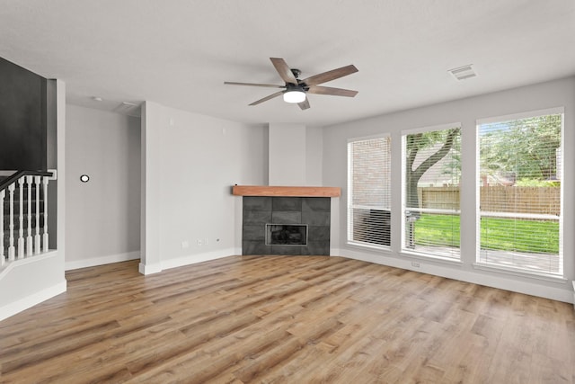 unfurnished living room featuring a tiled fireplace, a ceiling fan, baseboards, wood finished floors, and visible vents