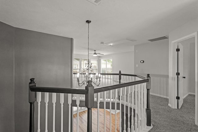 hallway with carpet flooring, a notable chandelier, baseboards, an upstairs landing, and visible vents