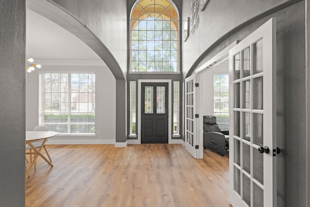 entryway featuring crown molding, arched walkways, french doors, baseboards, and wood finished floors