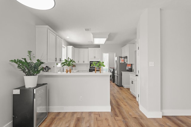 kitchen featuring freestanding refrigerator, a peninsula, white cabinetry, and visible vents