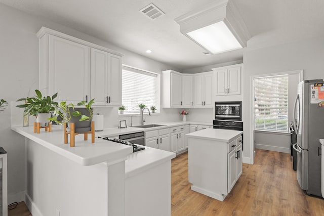 kitchen with a sink, built in microwave, freestanding refrigerator, white cabinetry, and visible vents